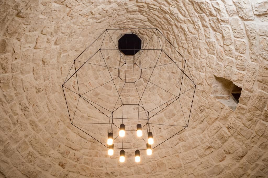 A hexagonal geometric light fixture suspended from a stone ceiling with a rough texture.