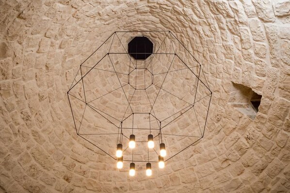 Una lámpara hexagonal de diseño geométrico, colgada del techo de piedra con textura rugosa.