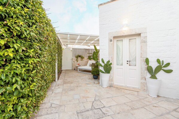 A paved courtyard with a white door, potted plants, and a white wall.