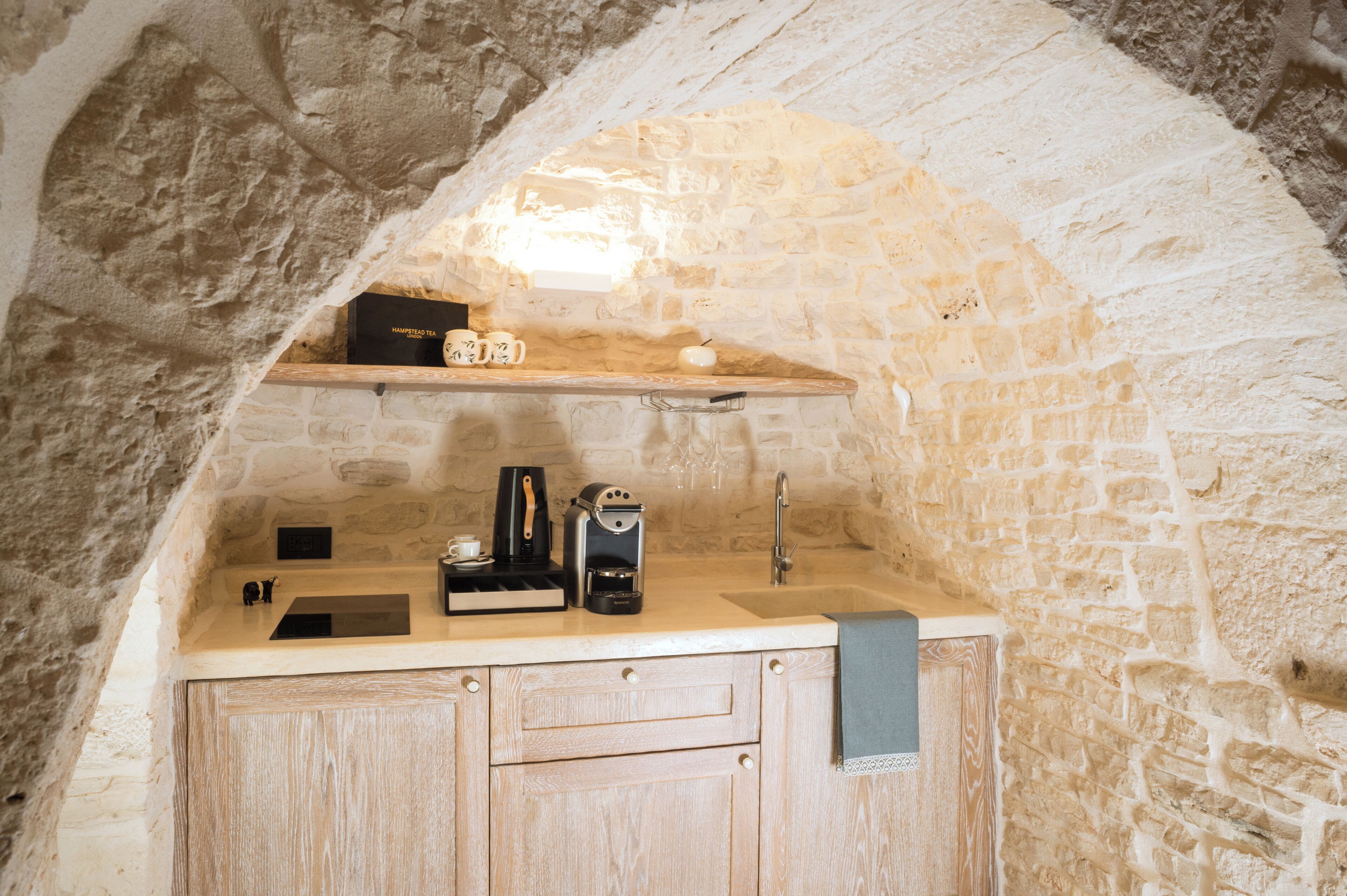 A stone-walled kitchen with a wooden countertop, a coffee machine, and a tea box labeled 'HAMPSTEAD TEA LONDON'.
