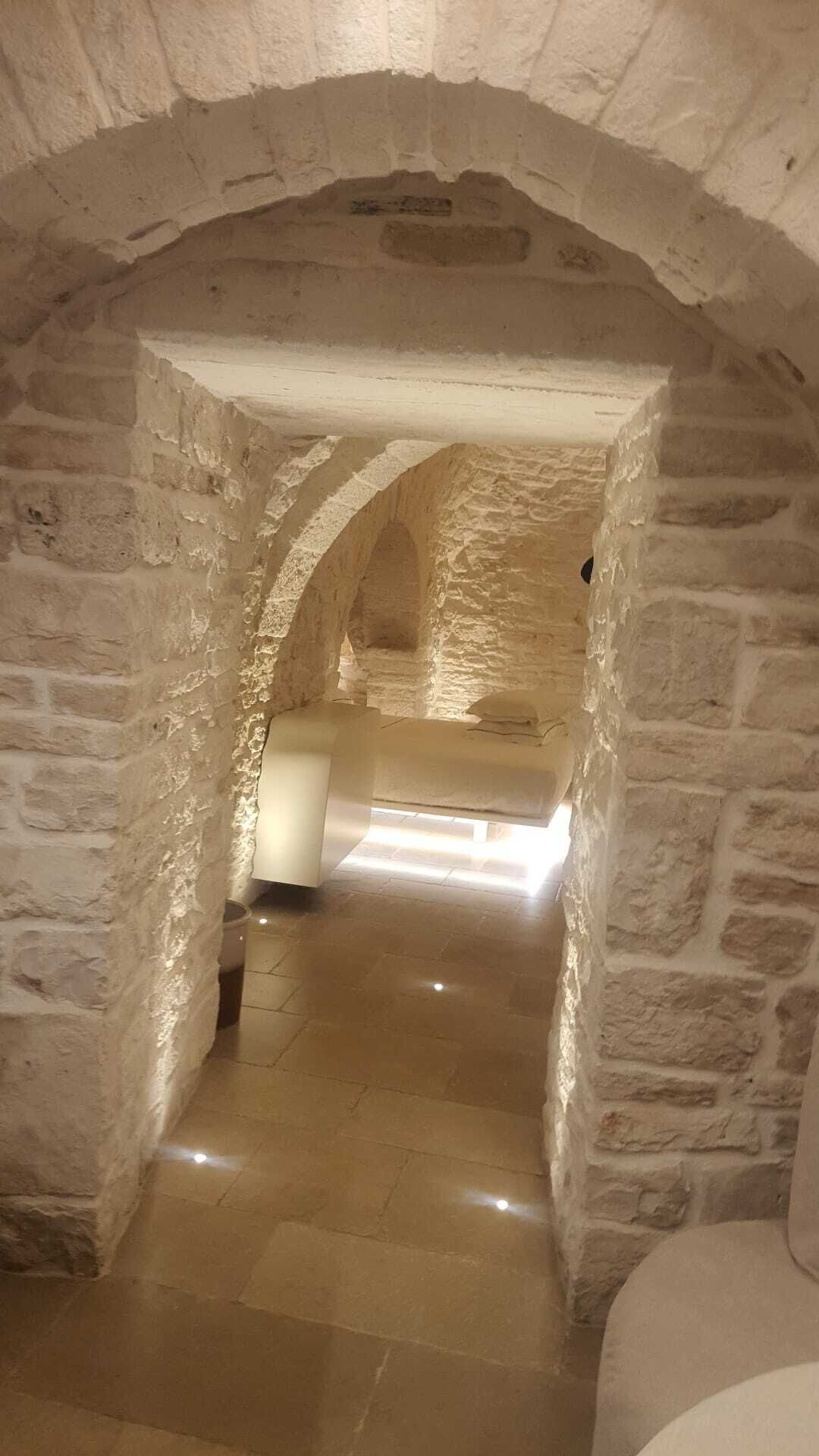 A stone-walled corridor with a bed at the end.