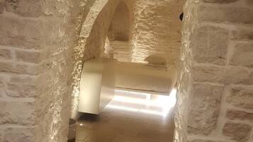 A stone-walled corridor with a bed at the end.