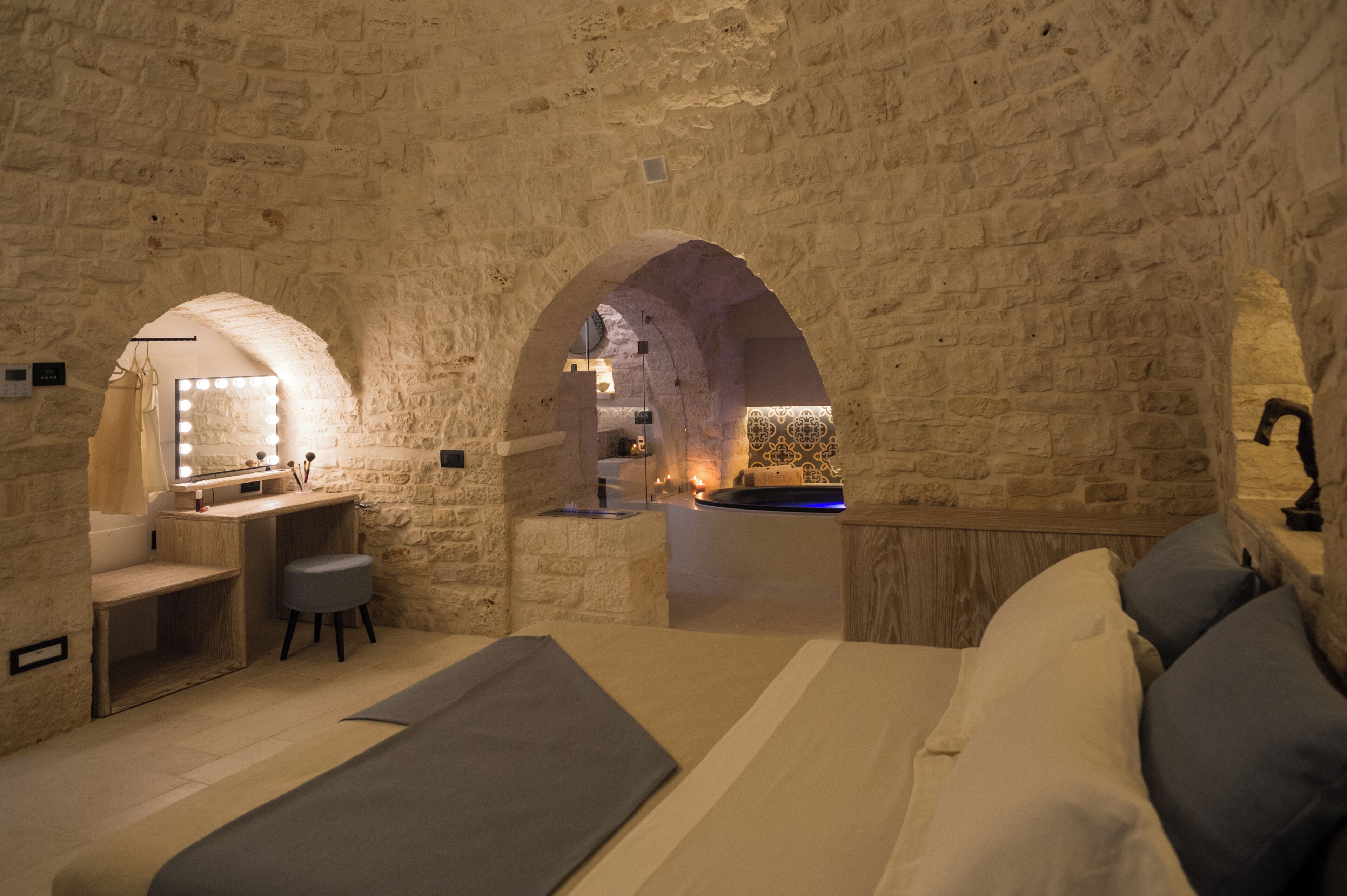 A stone-walled room with a bed, a vanity with a mirror, and a small seating area.