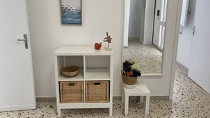Un couloir avec une console blanche, des paniers en osier, un petit tabouret et un miroir qui reflète l’intérieur.