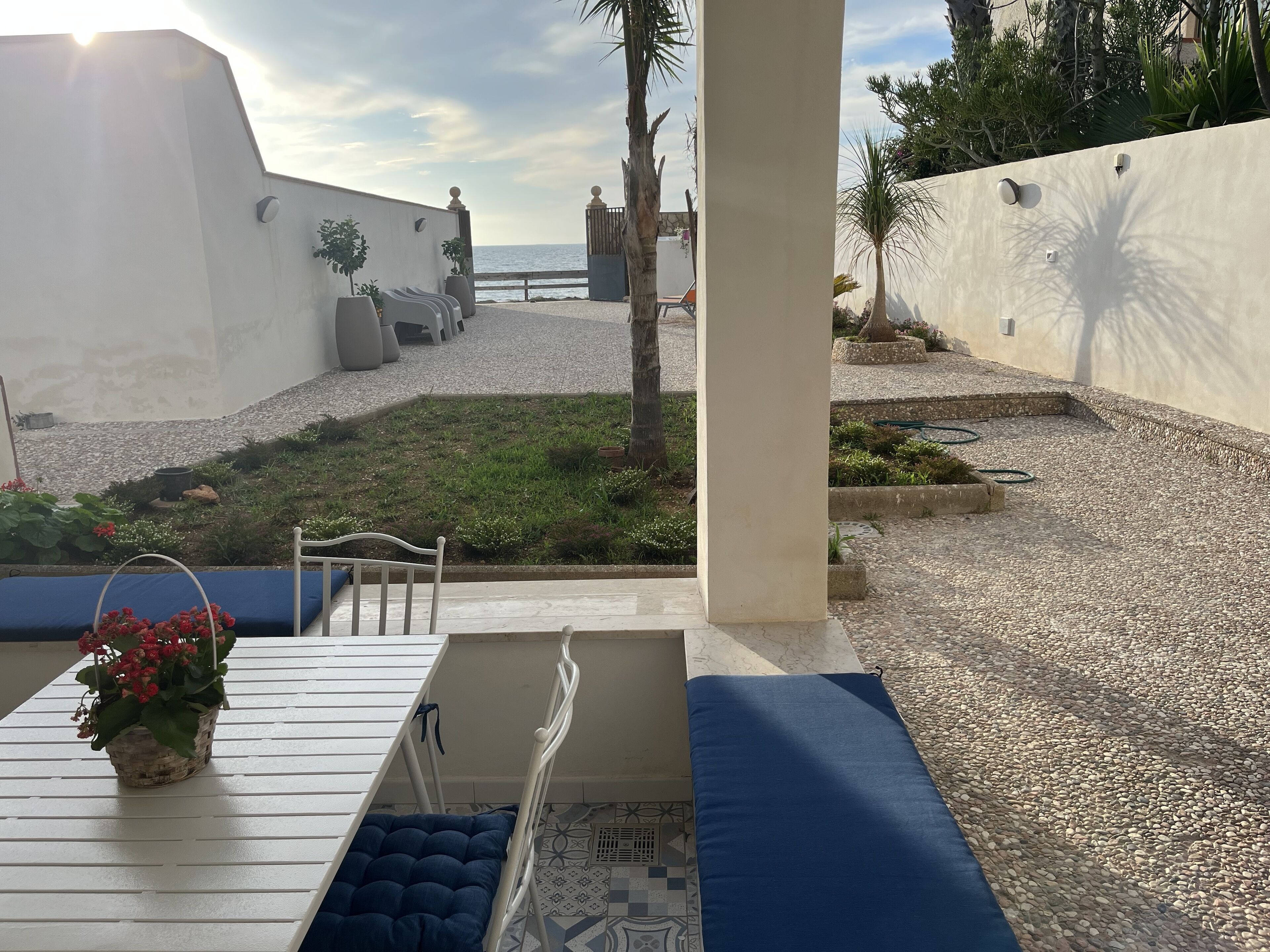 Una terrazza con vista sul mare, un muro bianco e un'area salotto con un cuscino blu.