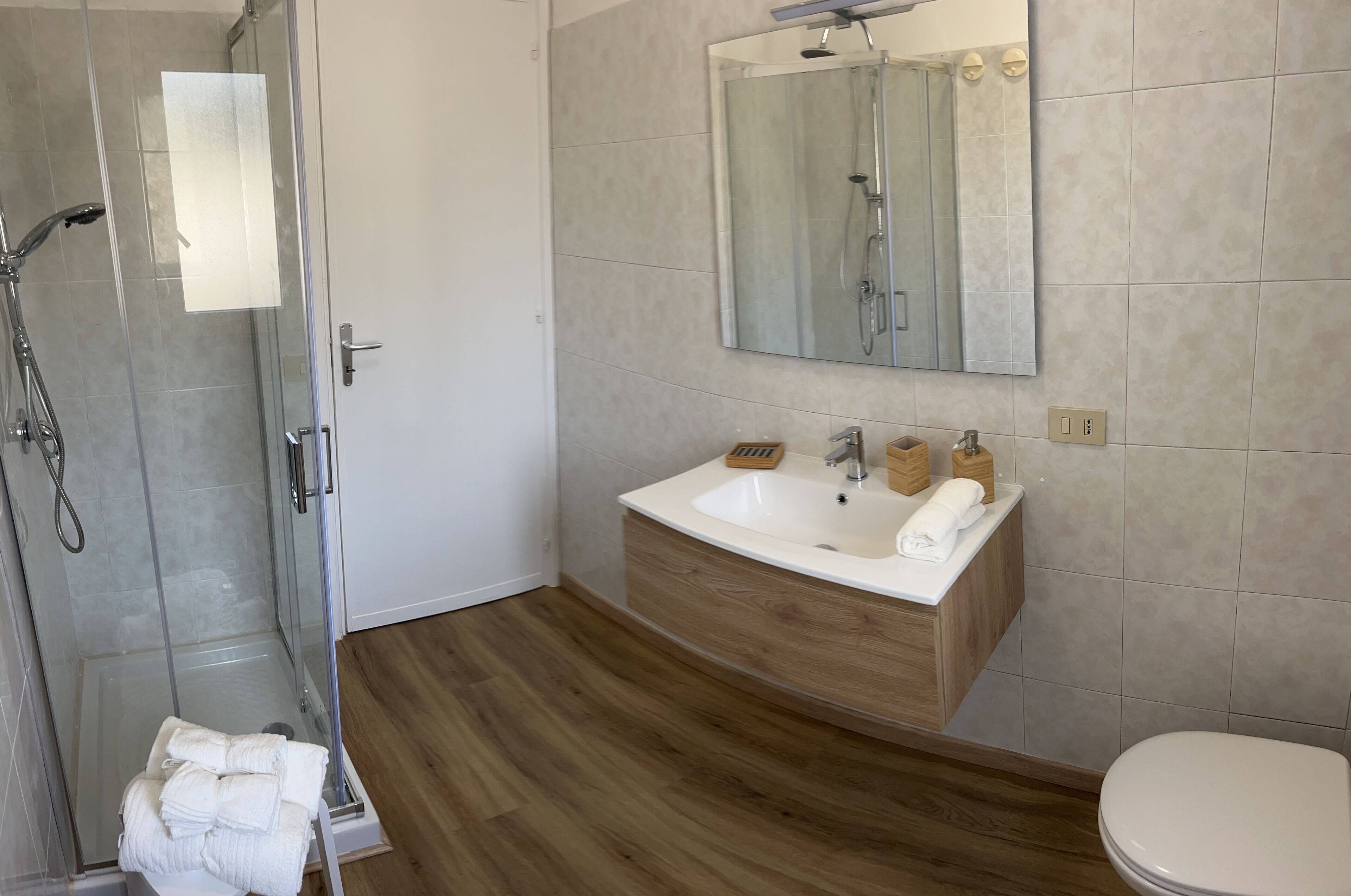 Ein modernes Badezimmer mit Duschkabine aus Glas, einem Holzkosmetikschrank mit Waschbecken und einer Toilette.