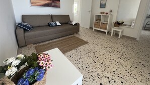 Un salon avec un canapé, une table basse ornée de fleurs, un tableau accroché au mur et un meuble blanc contenant des paniers.
