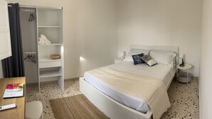 Une chambre à coucher avec un lit, une table de chevet avec une lampe, une armoire et une petite table sur laquelle se trouvent une balance et un livre.