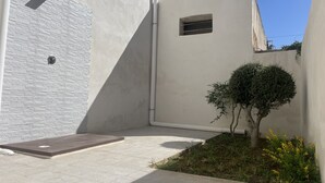 Un espace extérieur moderne avec un mur en briques blanches, un petit arbre et un jardinier orné de fleurs jaunes.