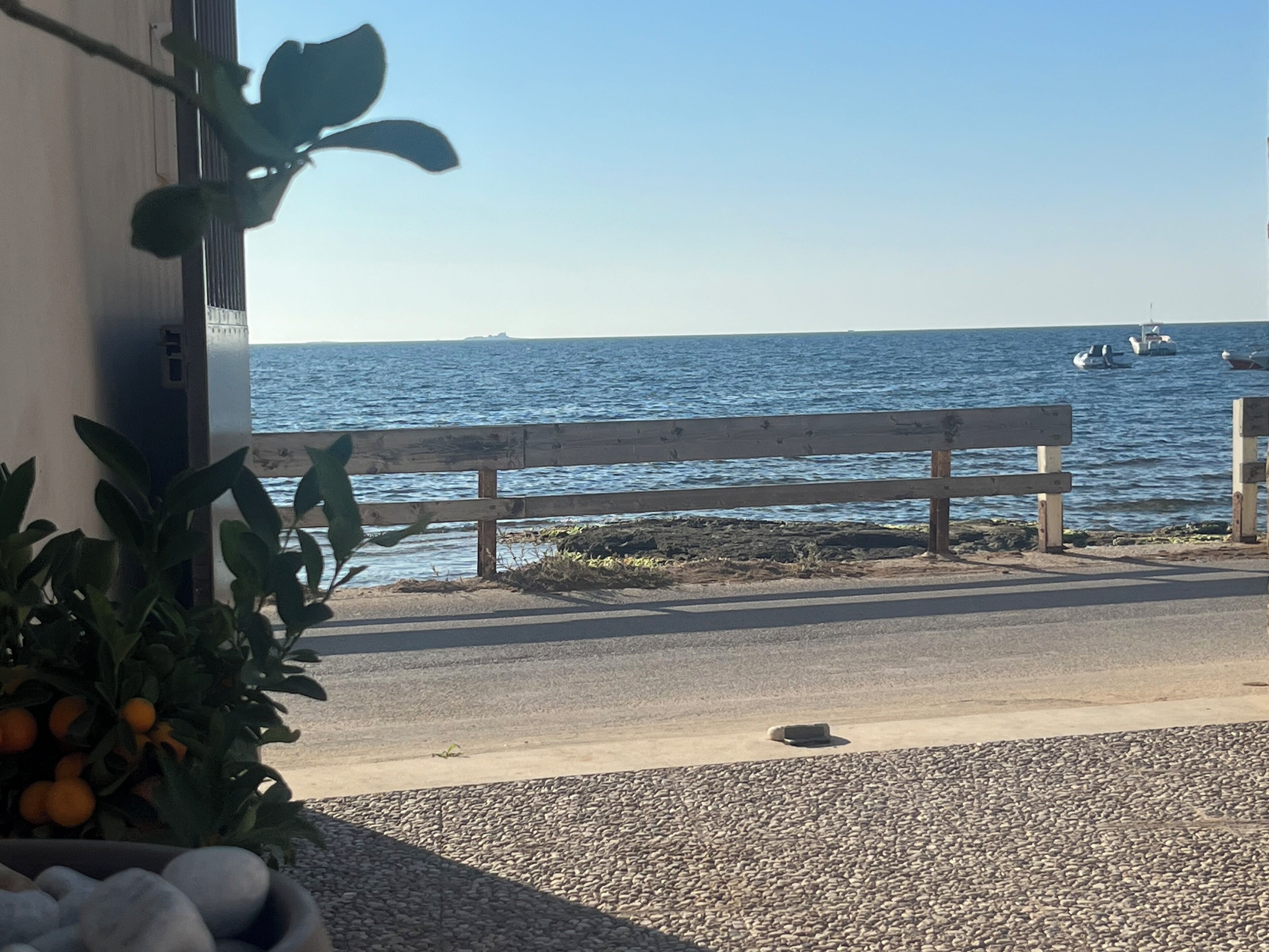 Een uitzicht op de kust met een houten bankje, een kiezelstrand en boten op het water.
