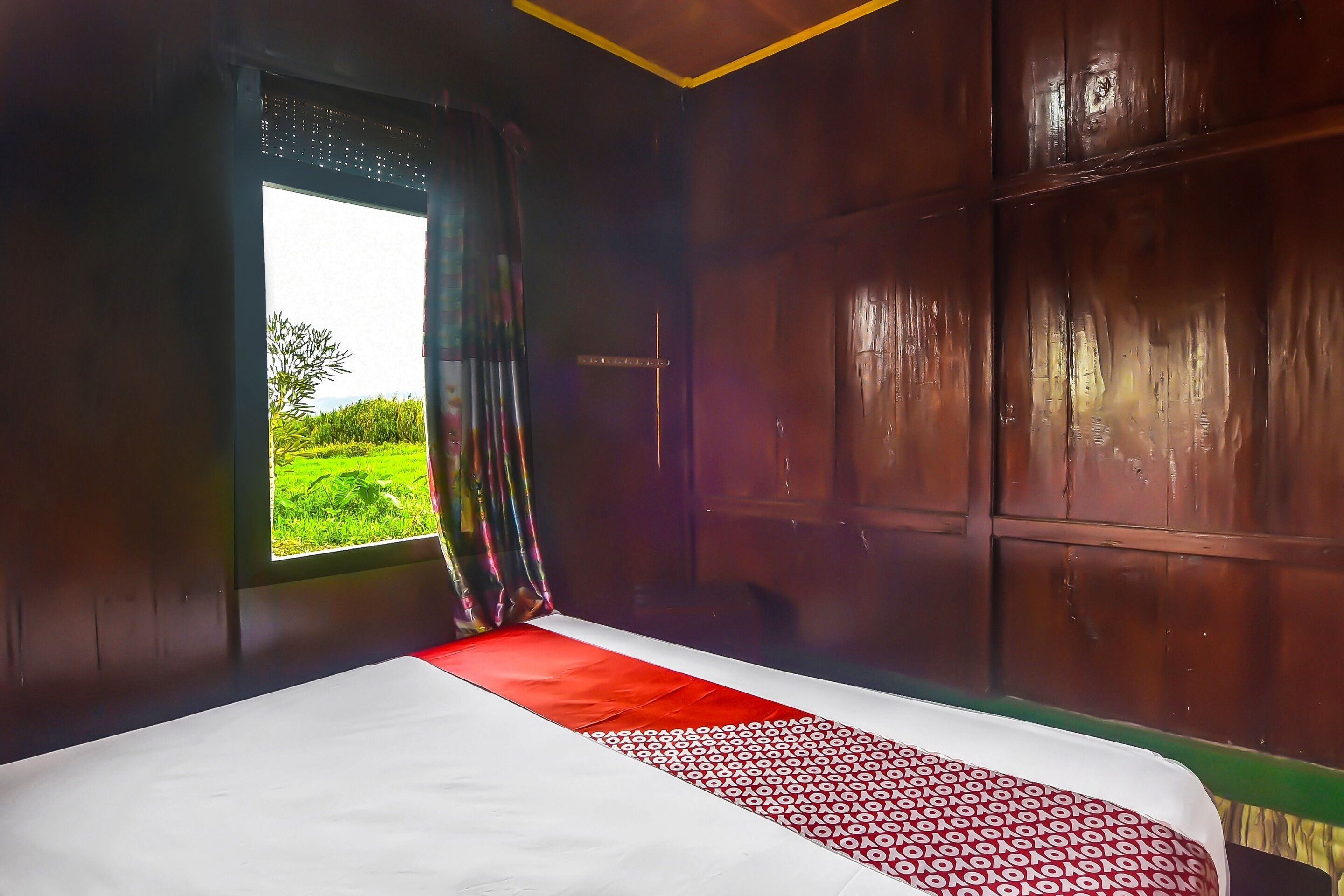 A room with a large bed, a window with curtains, and a view of greenery outside.