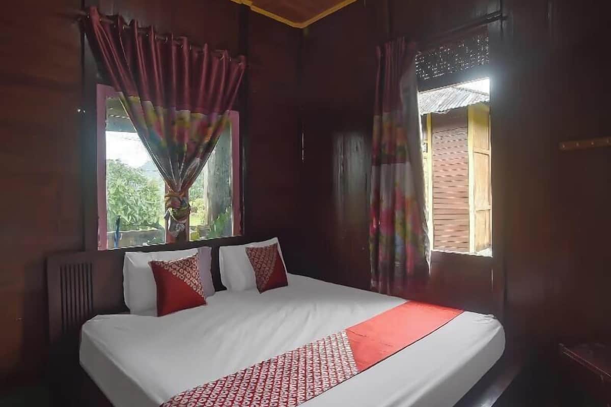 Un letto con biancheria bianca e dettagli rossi, una finestra con tende e un soffitto in legno.