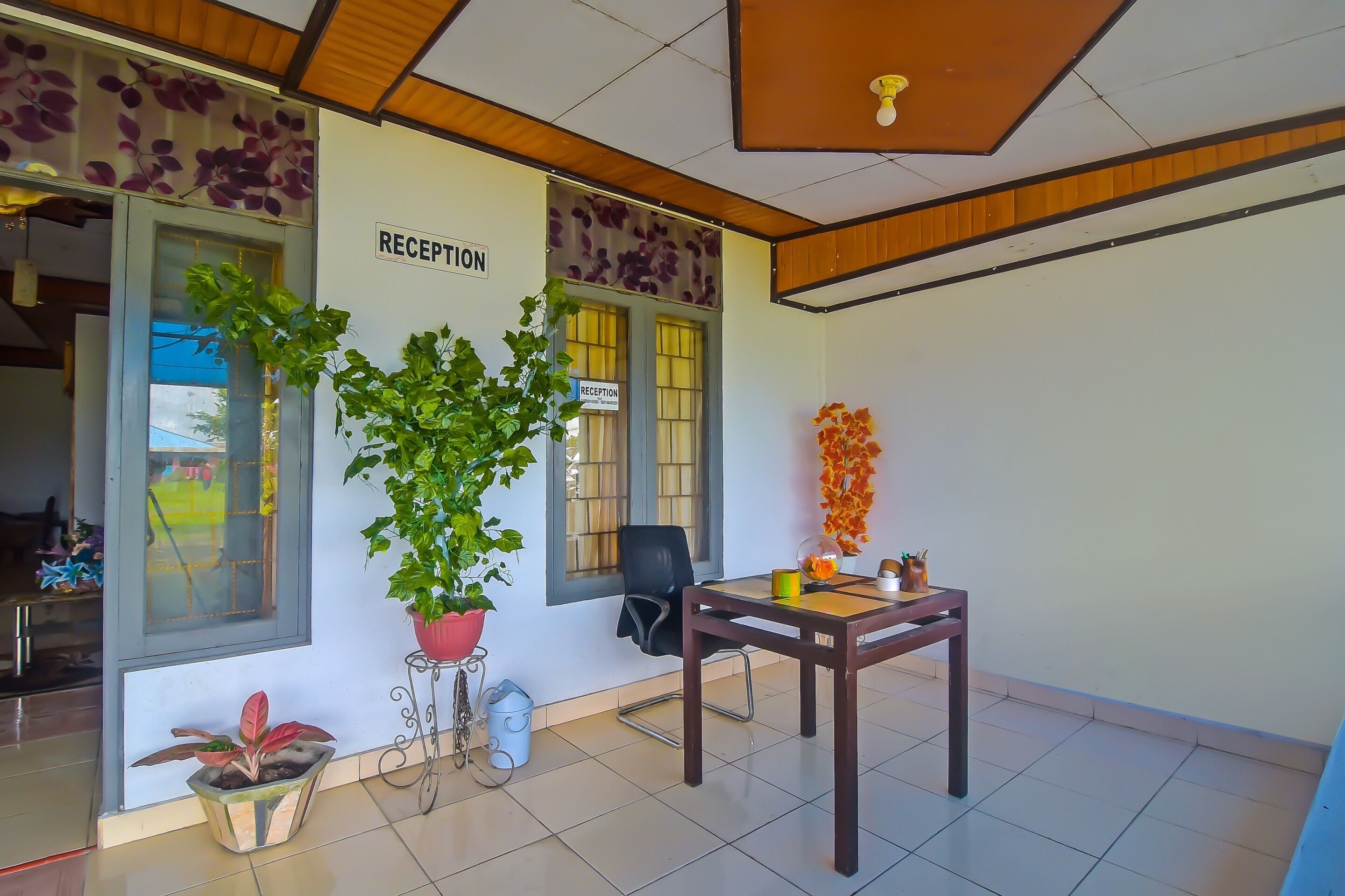 A reception area with a sign, a potted plant, a table with a chair, and a window with a view.