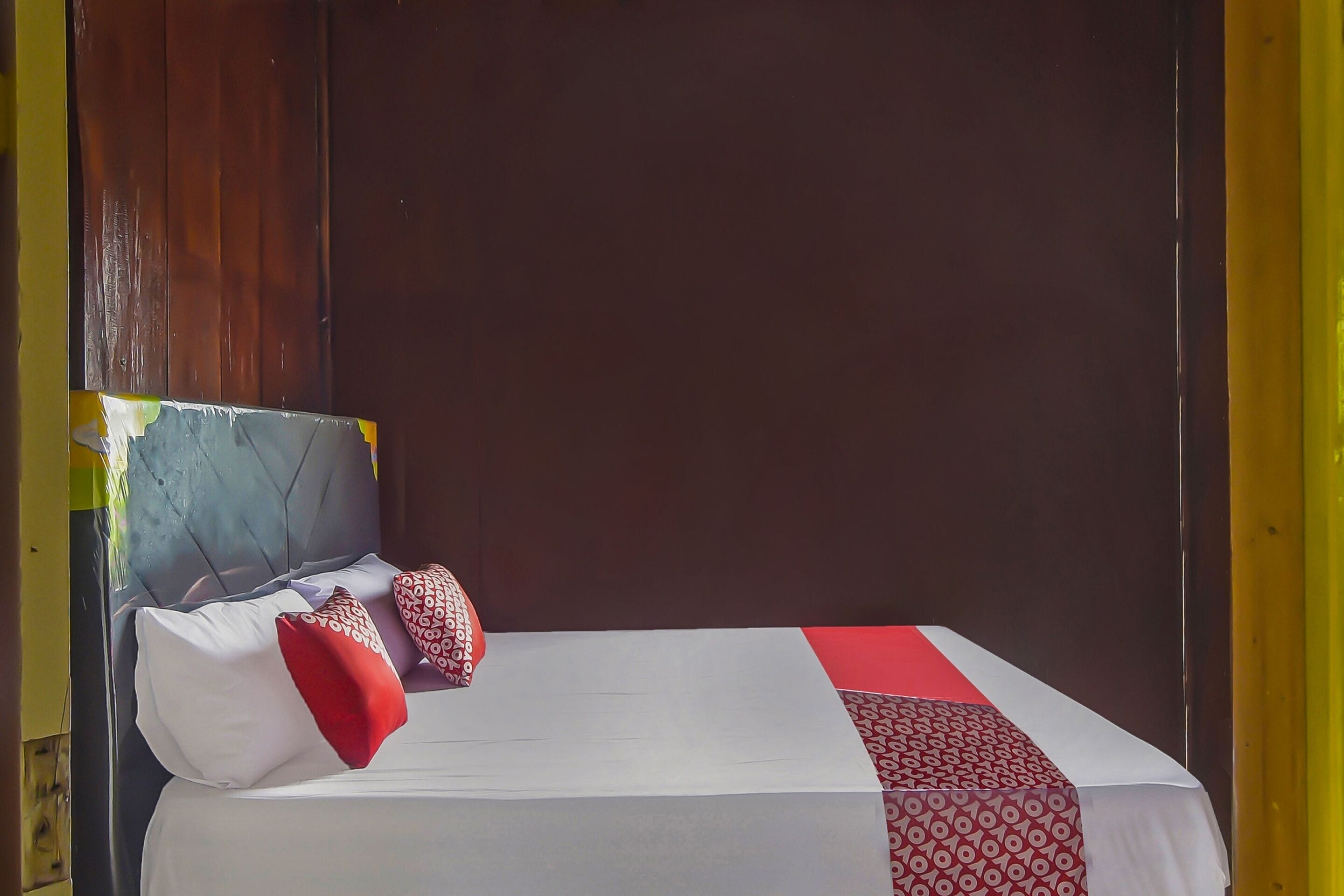 A bed with a white and red patterned bedspread, a wooden headboard, and two pillows.