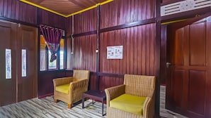 A room with wooden paneling, two wicker chairs with yellow cushions, a small table, and a door with a sign on it. - Hotel O Filadelfia Resto & Penginapan Near Benteng Moraya (Manado)