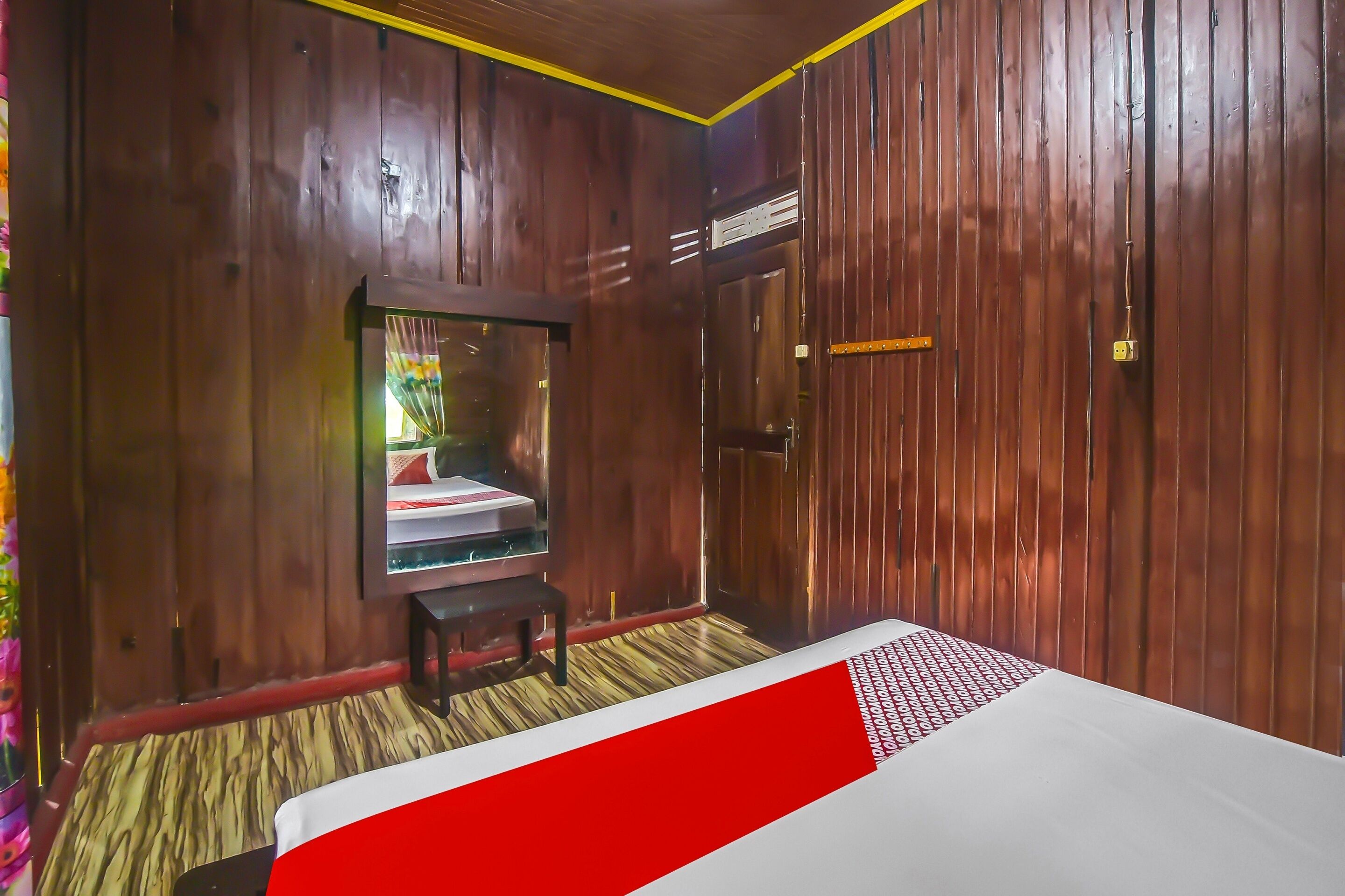 Una habitación con paredes de madera, una cama con colcha blanca y roja, una mesita y un espejo.
