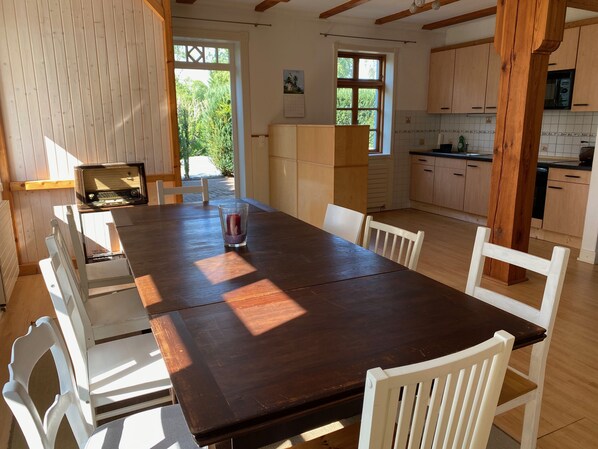 Una mesa de comedor de madera con sillas, un candelabro de vidrio y una vista de una cocina con armarios de madera y un ventanal.