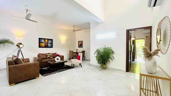 A spacious living room with a sofa, coffee table, and chairs, a dining area with a table and chairs, and a large potted plant.