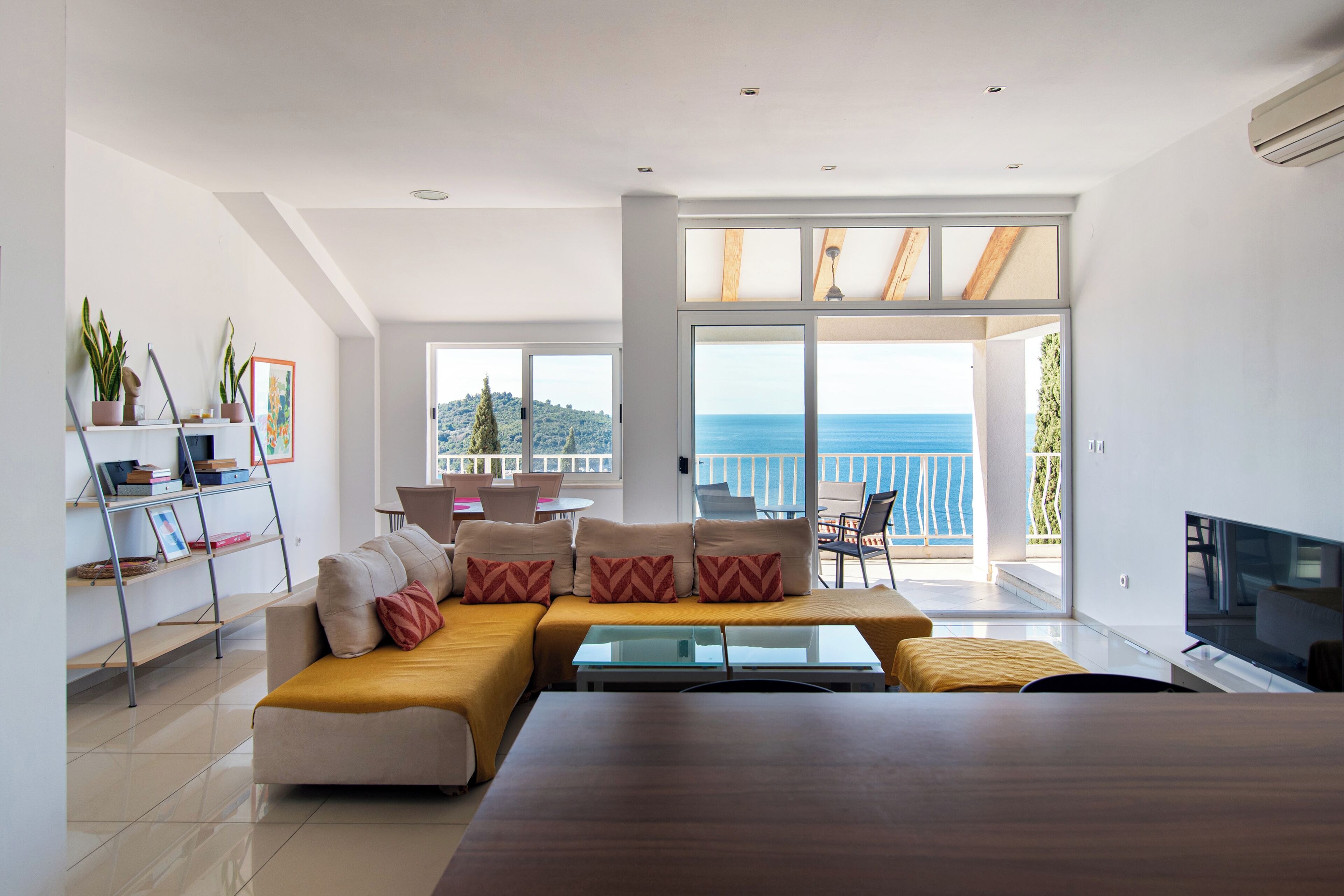 Un salon moderne avec un canapé, une table basse, un téléviseur et un balcon offrant une vue sur la mer.