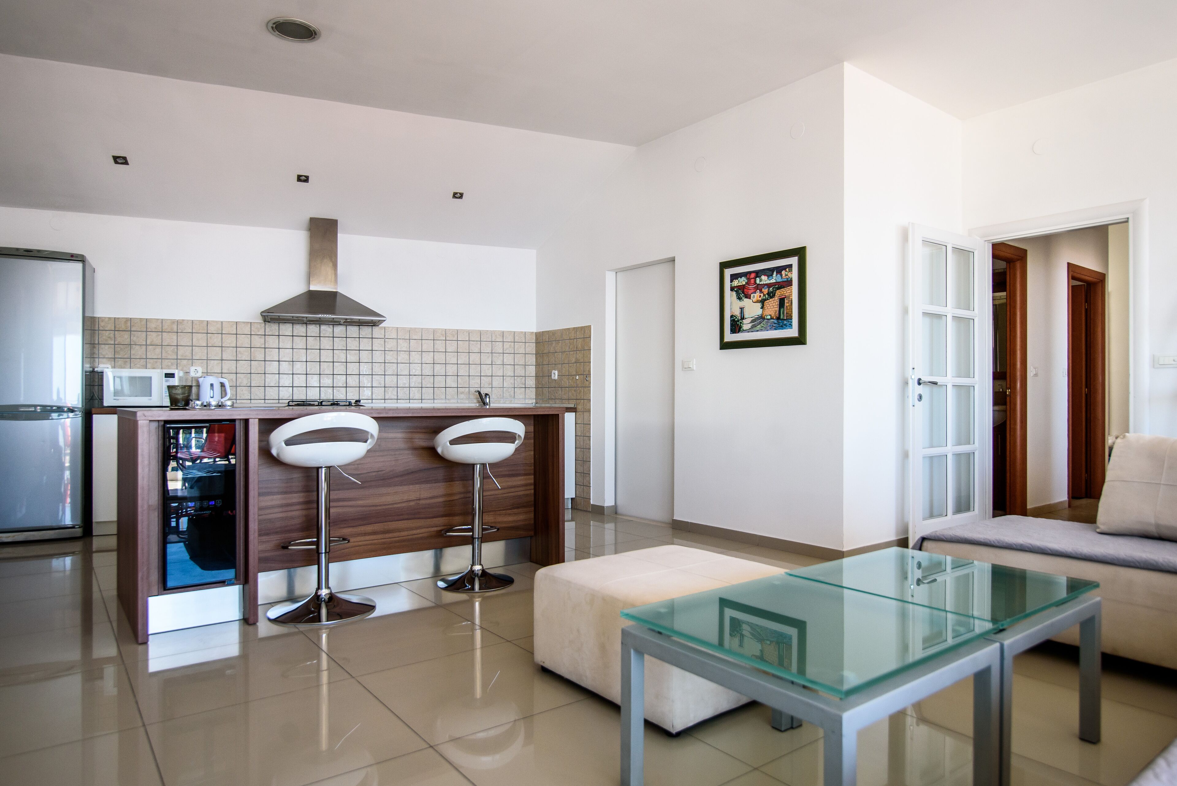 A modern kitchen with a built-in microwave, a stainless steel range hood, and a wooden countertop. There are two bar stools and a glass-top table.
