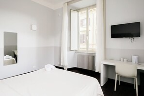 A hotel room with a bed, a desk, a chair, a TV, and a window with curtains.