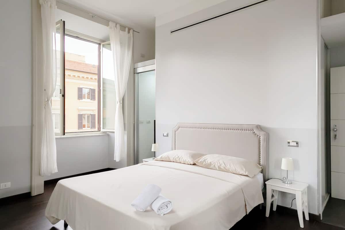 Ein Hotelzimmer mit einem großen Bett, einem Nachttisch mit Lampe und einem Fenster mit Vorhängen.