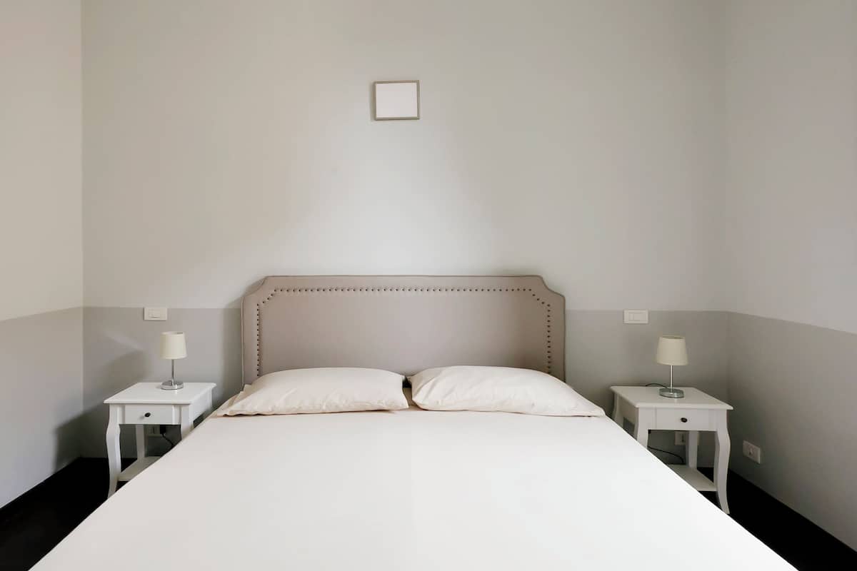 Ein ordentlich bezogenes Bett mit Kopfteil, zwei Nachttische mit Lampen und ein kleiner Bilderrahmen an der Wand.