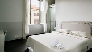 A hotel room with a bed, a window with curtains, a bedside table, and a view of buildings outside. - DM69 - Termini Monti Crossroads (Rome)