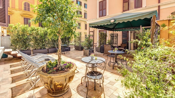 An outdoor patio area with seating arrangements, a large planter with a tree, and a covered seating area with a green awning. - DM69 - Termini Monti Crossroads (Rome)
