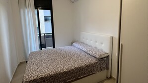 Un dormitorio con cama, ventana con cortinas, equipo de aire acondicionado y una puerta.