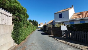 A narrow residential street with houses on both sides, a wooden fence, and a clear blue sky. - Cozy cottage near beach, 4 pax, private parking (La Faute-sur-Mer)