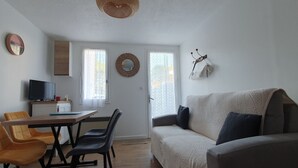 A living room with a sofa, chairs, a dining table, and a television. - Cozy cottage near beach, 4 pax, private parking (La Faute-sur-Mer)