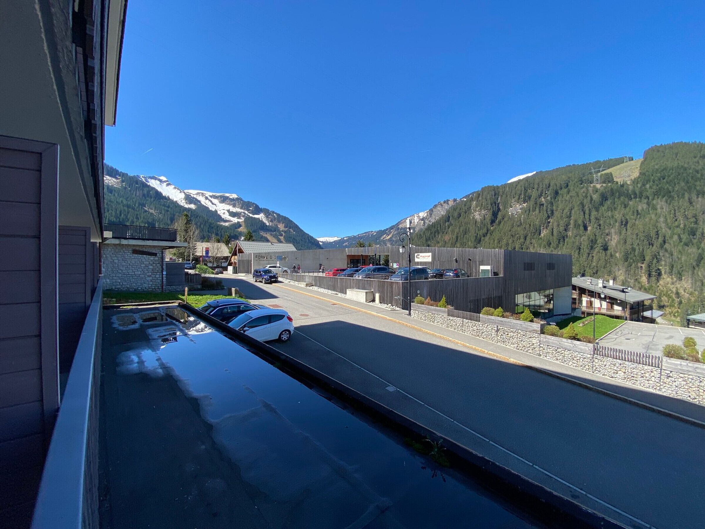 A modern building with a parking lot and a view of snow-capped mountains.