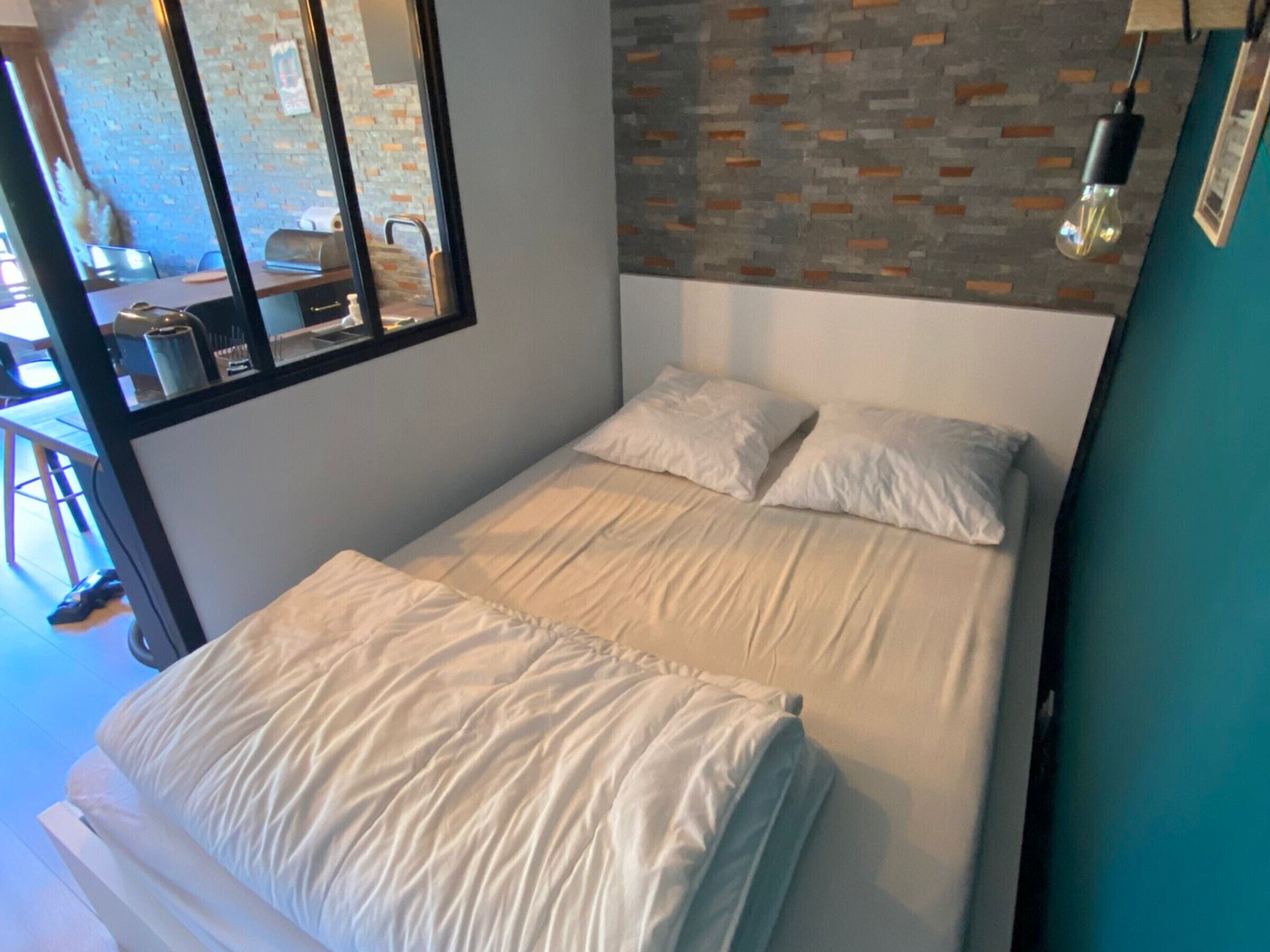 A bedroom with a bed, two pillows, a window, and a brick-patterned wall.