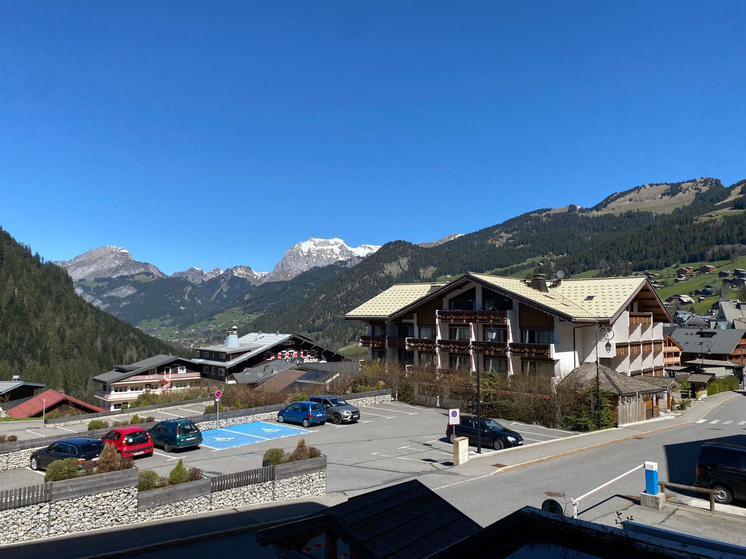 Une ville de montagne avec un parking, un bâtiment doté d’un toit en pente et, en arrière-plan, des montagnes enneigées.