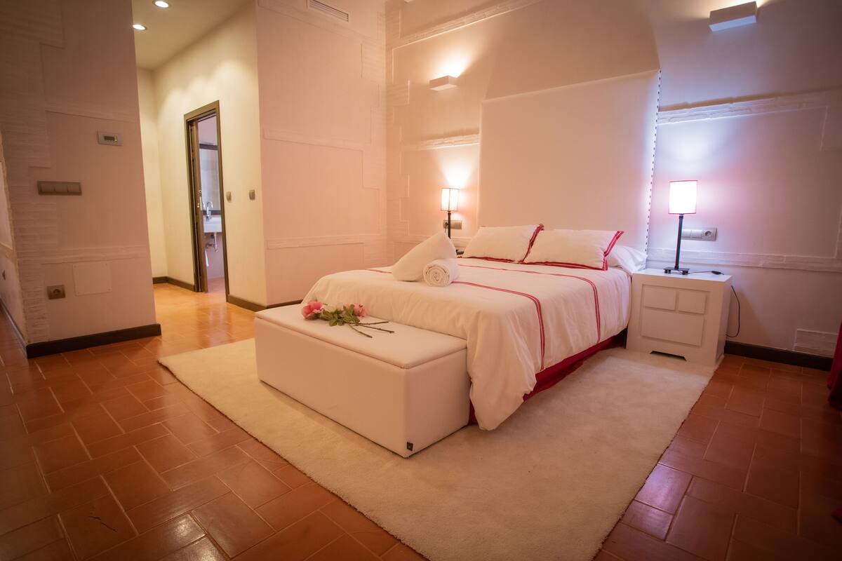 Un dormitorio con cama, mesitas de noche, un banco y una alfombra.