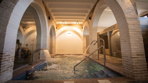 Ein Wellnessbereich mit Whirlpool, gewölbten Ziegelstützen und gefliestem Boden.