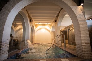Un espacio de spa con un hidromasaje, columnas de ladrillo en arco y suelo de baldosas.