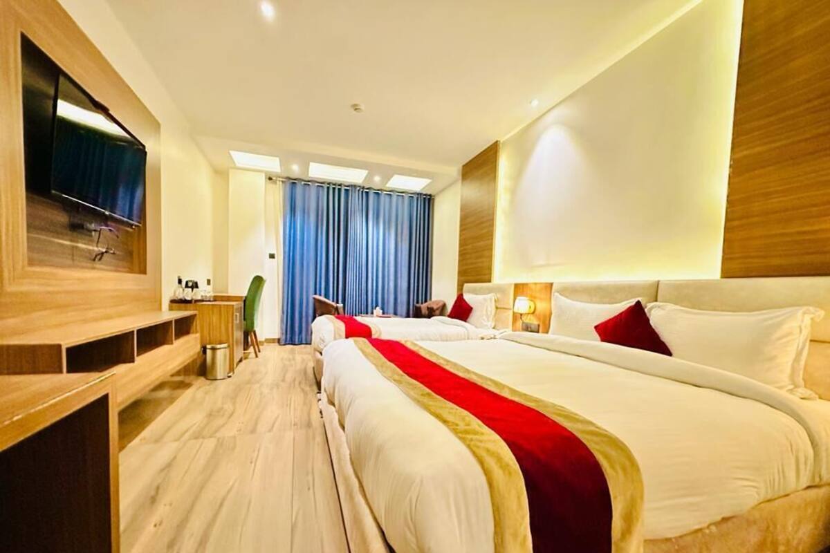 A hotel room with a large bed, a TV mounted on the wall, a desk with a chair, and a view of the outside through a window.