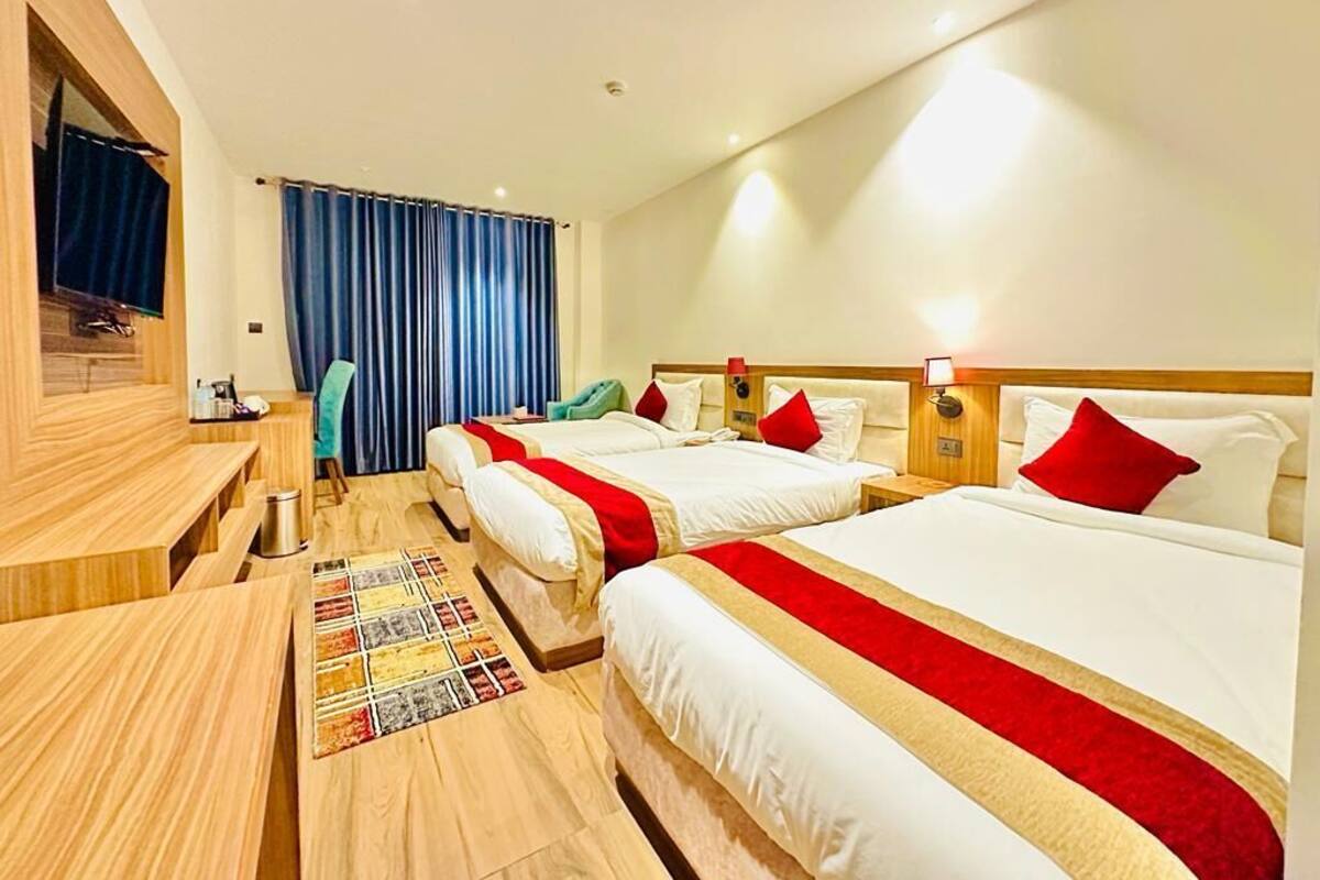 A hotel room with three beds, a TV, a desk, and a window with curtains.