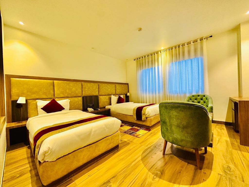 Habitación de hotel con dos camas, un sillón verde y suelo de madera.