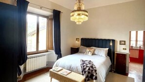 Ein Schlafzimmer mit einem großen Bett, einer hängenden Chandelier, einem Fenster mit Vorhängen und einem Heizkörper.