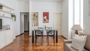 Een moderne woonkamer met een eetgedeelte, houten vloeren en een bank met geborduurde kussens.