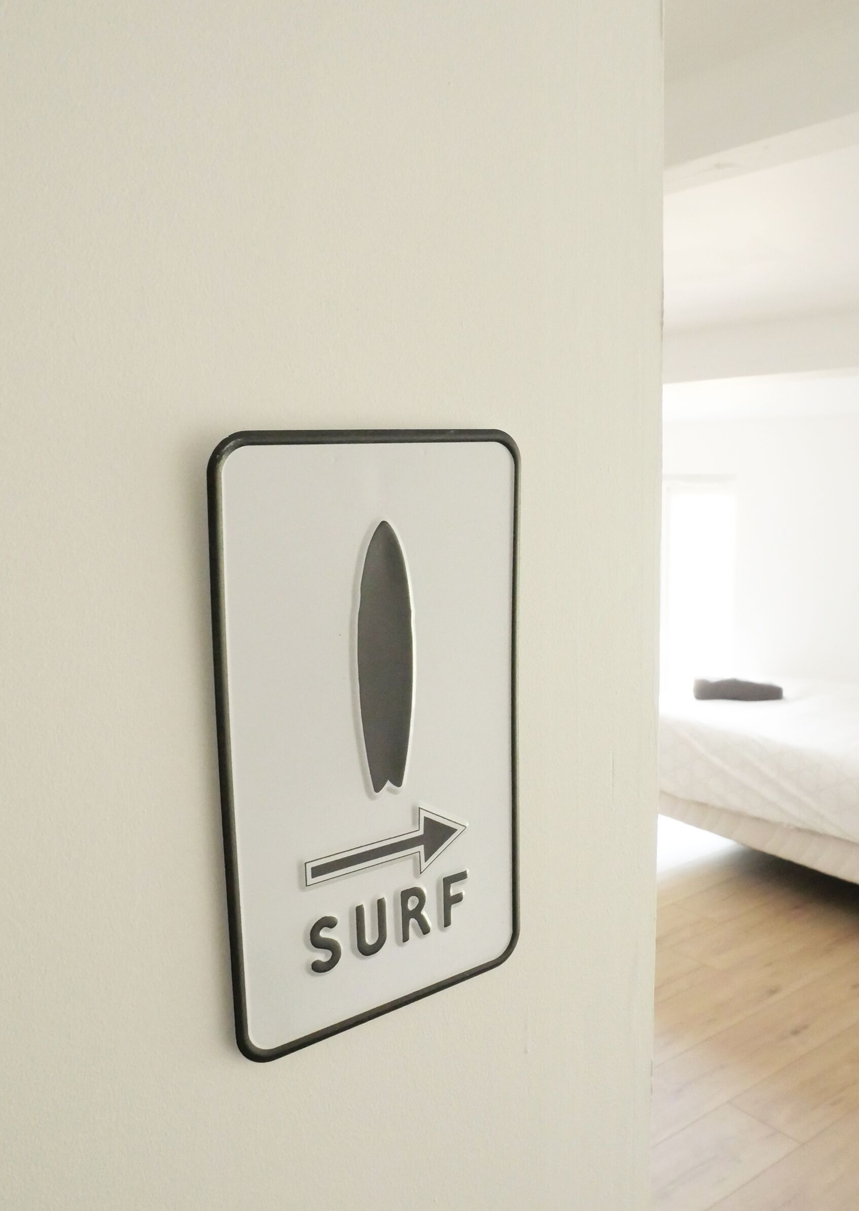 Une enseigne fixée au mur, ornée d’un pictogramme de planche de surf et du mot « SURF », pointant vers la droite, indiquant un lieu ou une direction liés au surf.
