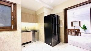 A modern kitchen with a black refrigerator, wooden cabinets, and a dishwasher. - BluO 3BHK CityWalk Mall, MAX Saket -Lift, Balcony (New Delhi)