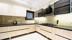 A modern kitchen with light wood cabinets, a black countertop, and a built-in stove. - BluO 3BHK CityWalk Mall, MAX Saket -Lift, Balcony (New Delhi)