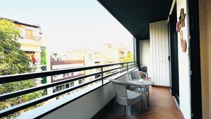 A balcony with a wicker table and chairs, a small potted plant, and a view of neighboring buildings. - BluO 3BHK CityWalk Mall, MAX Saket -Lift, Balcony (New Delhi)