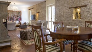 A spacious living room with a stone wall, a fireplace, and a dining area with a round table and chairs. - Villa San Marco - Homelike Villas (Torre San Marco)