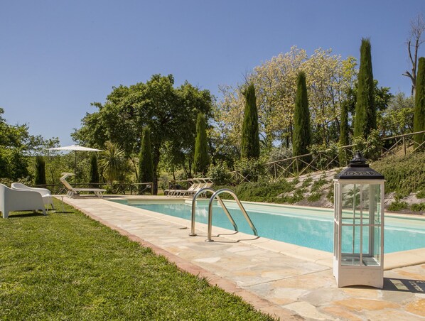 A swimming pool with a stone deck, surrounded by grass and trees.