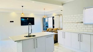 A modern kitchen with white cabinetry, a central island with a sink, pendant lighting, and a flat-screen TV mounted above the island.
